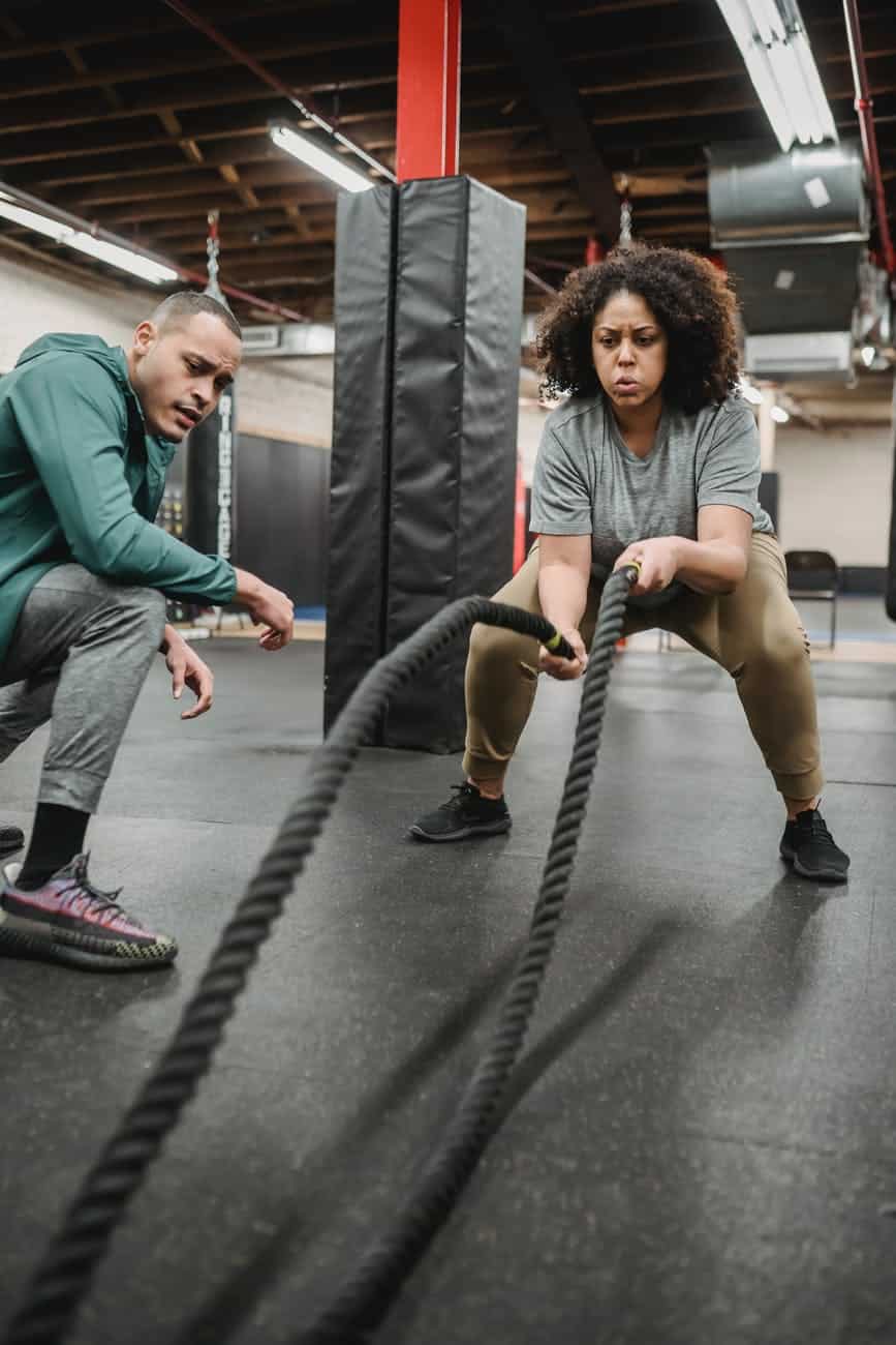concentrated black woman exercising with battle ropes in contemporary gym