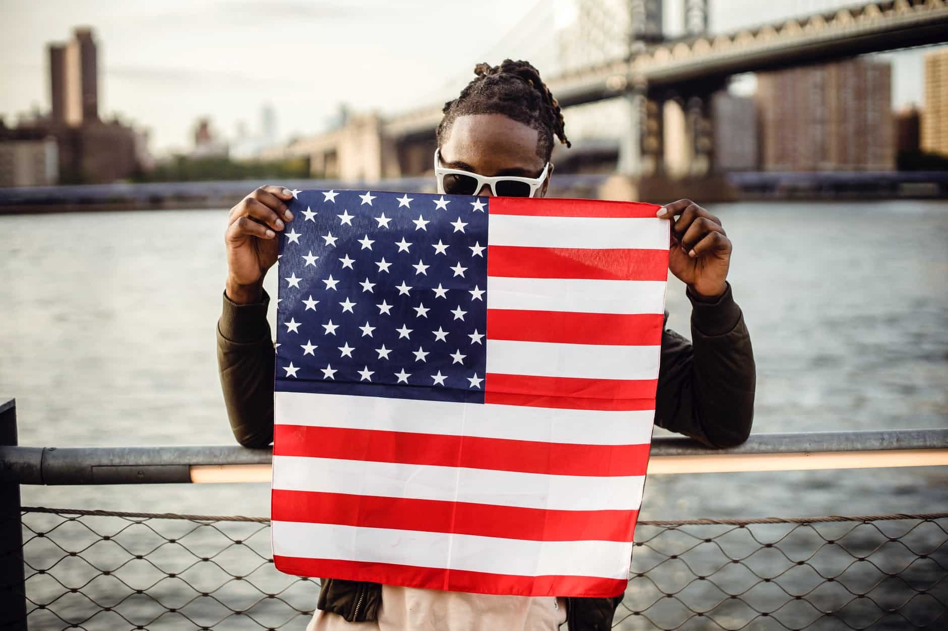 black man holding american flag on city river embankment